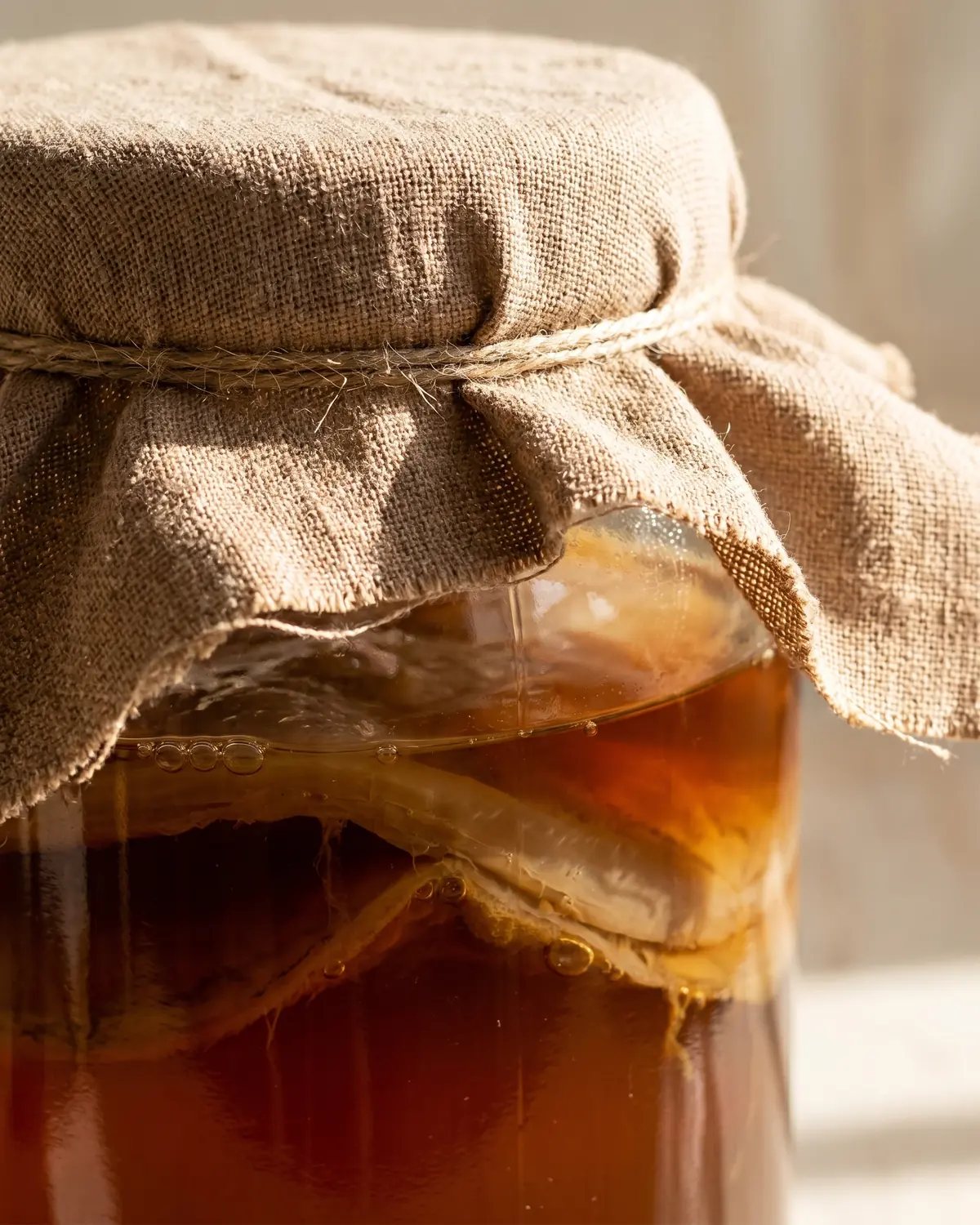 para qué es bueno la kombucha Primer plano de un tarro de kombucha cubierto con paño de algodón y té oscuro bajo la tela.