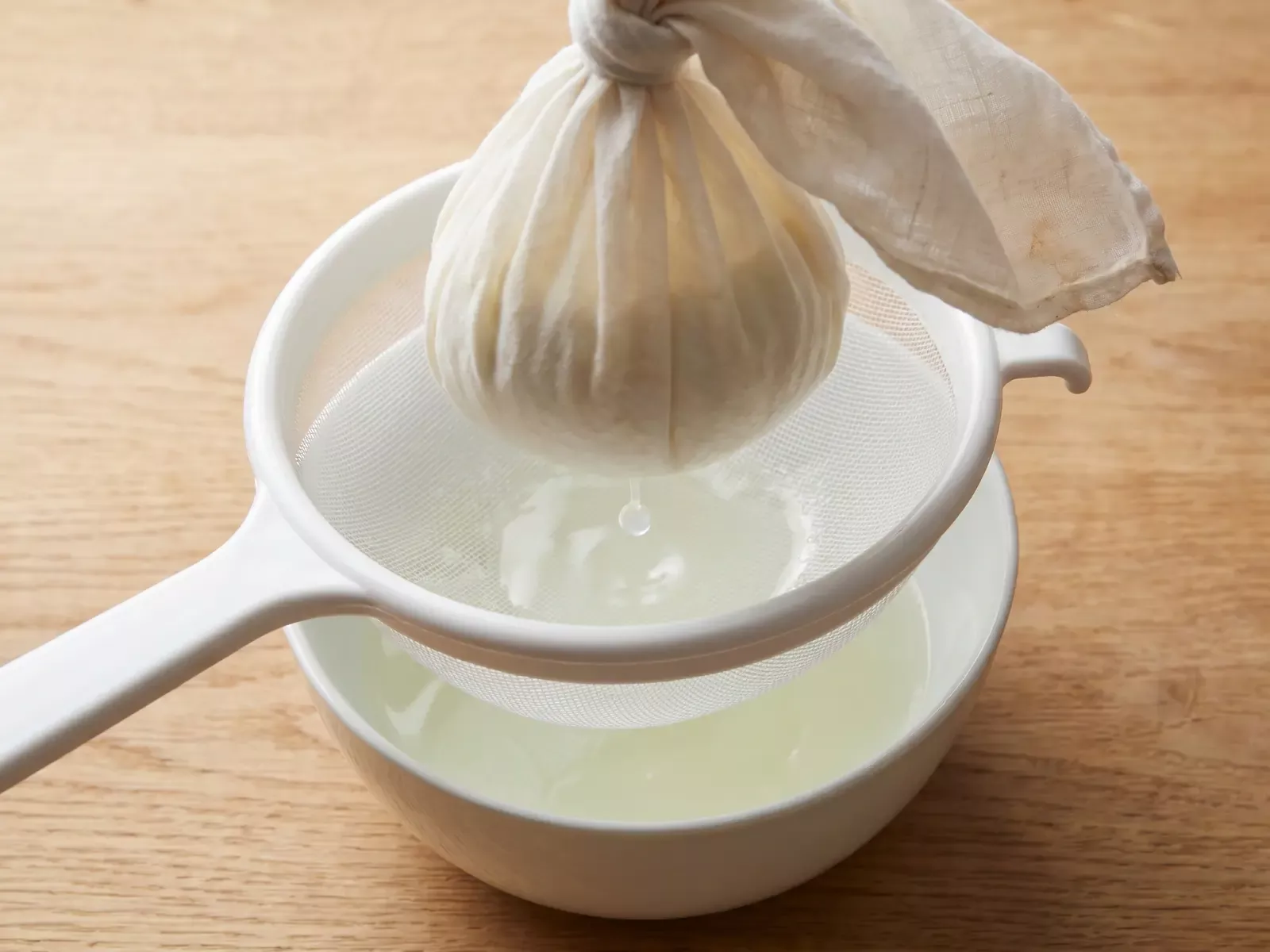 Yogur escurri&eacute;ndose en un colador con tela mientras una gota de suero cae lentamente.